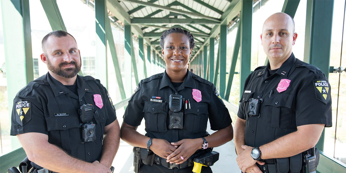 Three law enforcement officers wearing pink awareness badges.
